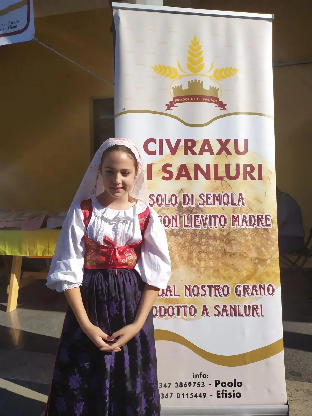 Bambina in costume tradizionale sardo accanto al marchio Civraxu di Sanluri