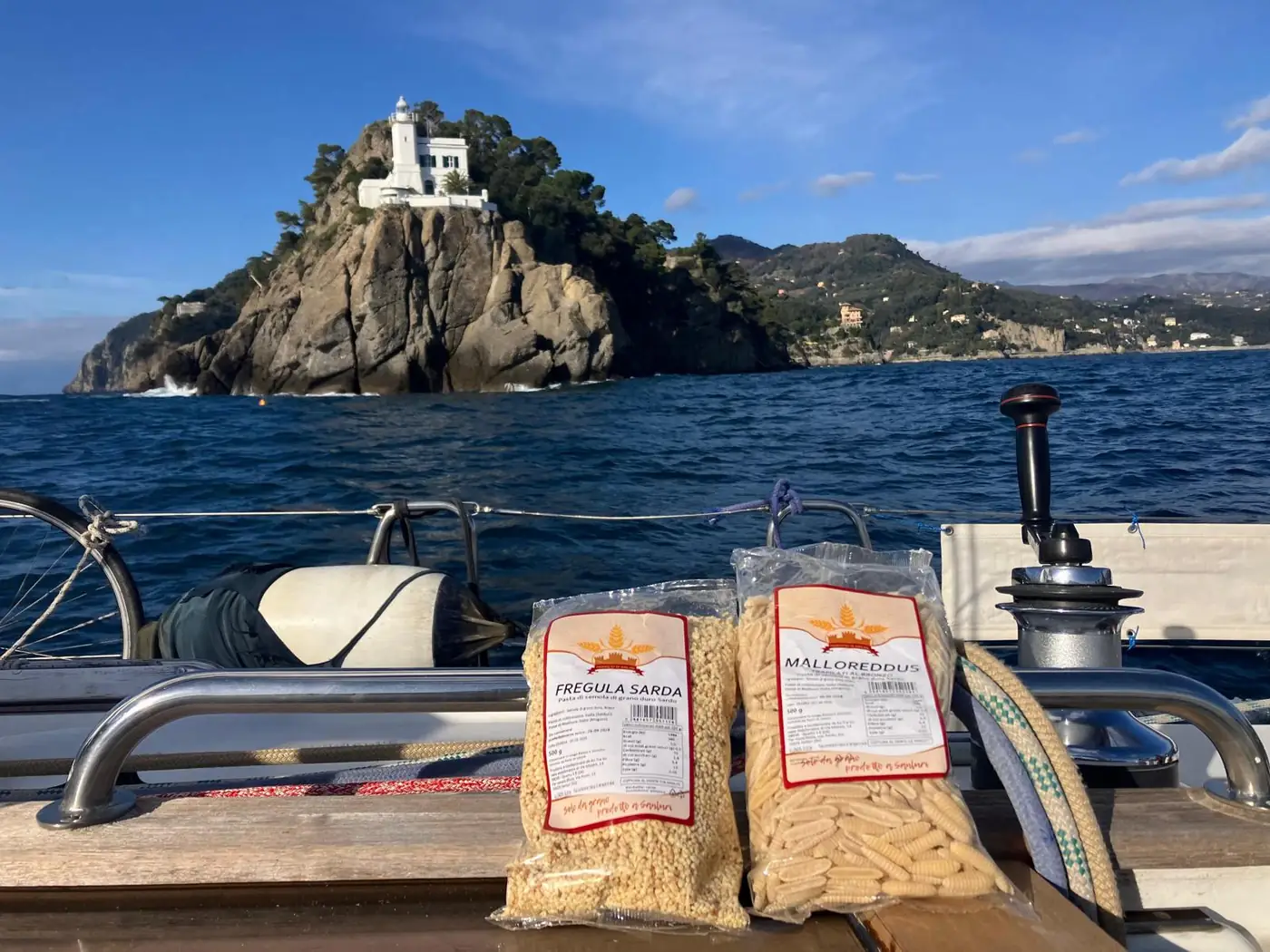 Fregula sarda e malloreddus a bordo di una barca a vela, con un faro sullo sfondo